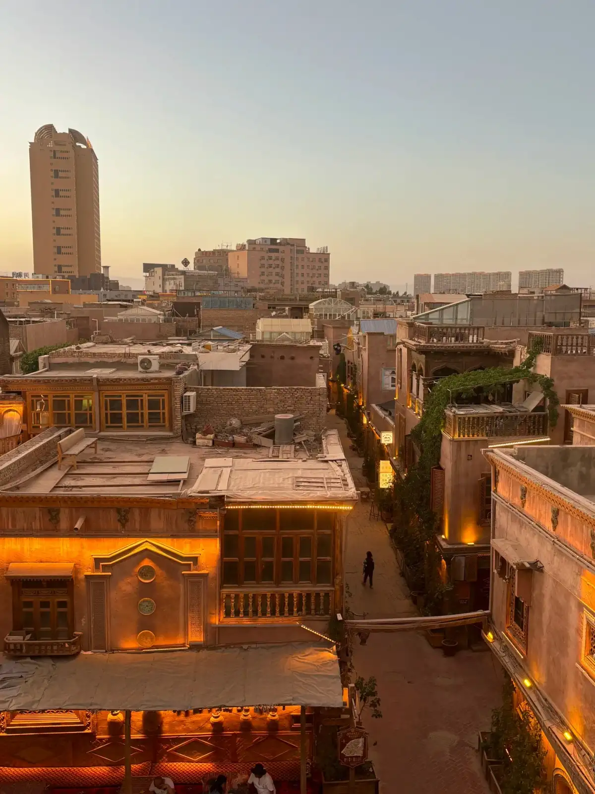 The old city’s rooftops, narrow alleys, and distant high-rises bathed in the warm glow of evening lights