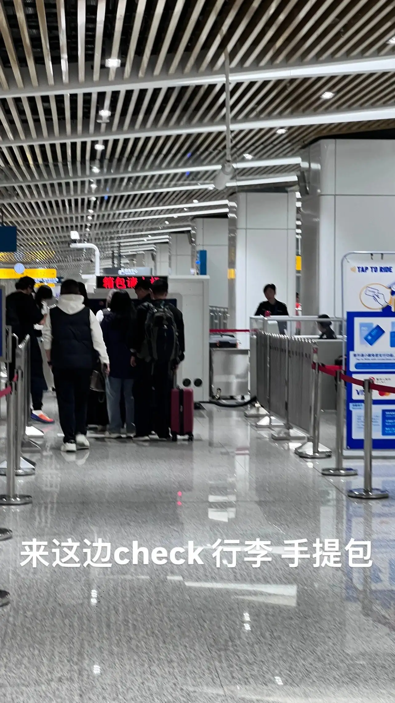 旅客带着行李进入站内检查通道，金属栏杆分隔通行区域。