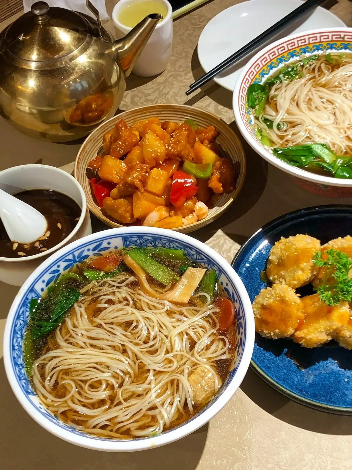 A table setting featuring a noodle bowl, a vegetable bowl, and a metal teapot