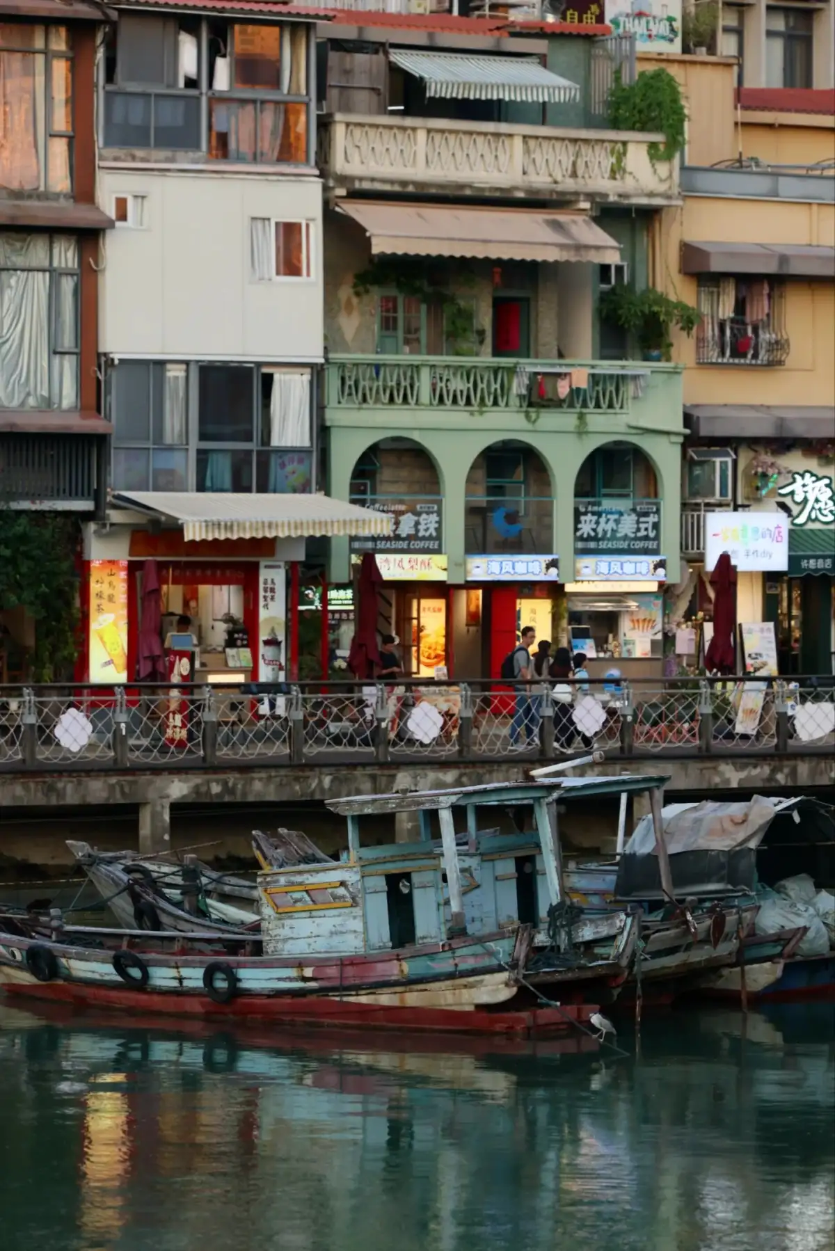 A wooden boat is moored in the foreground, with tiered houses, balconies, and shops in the background.