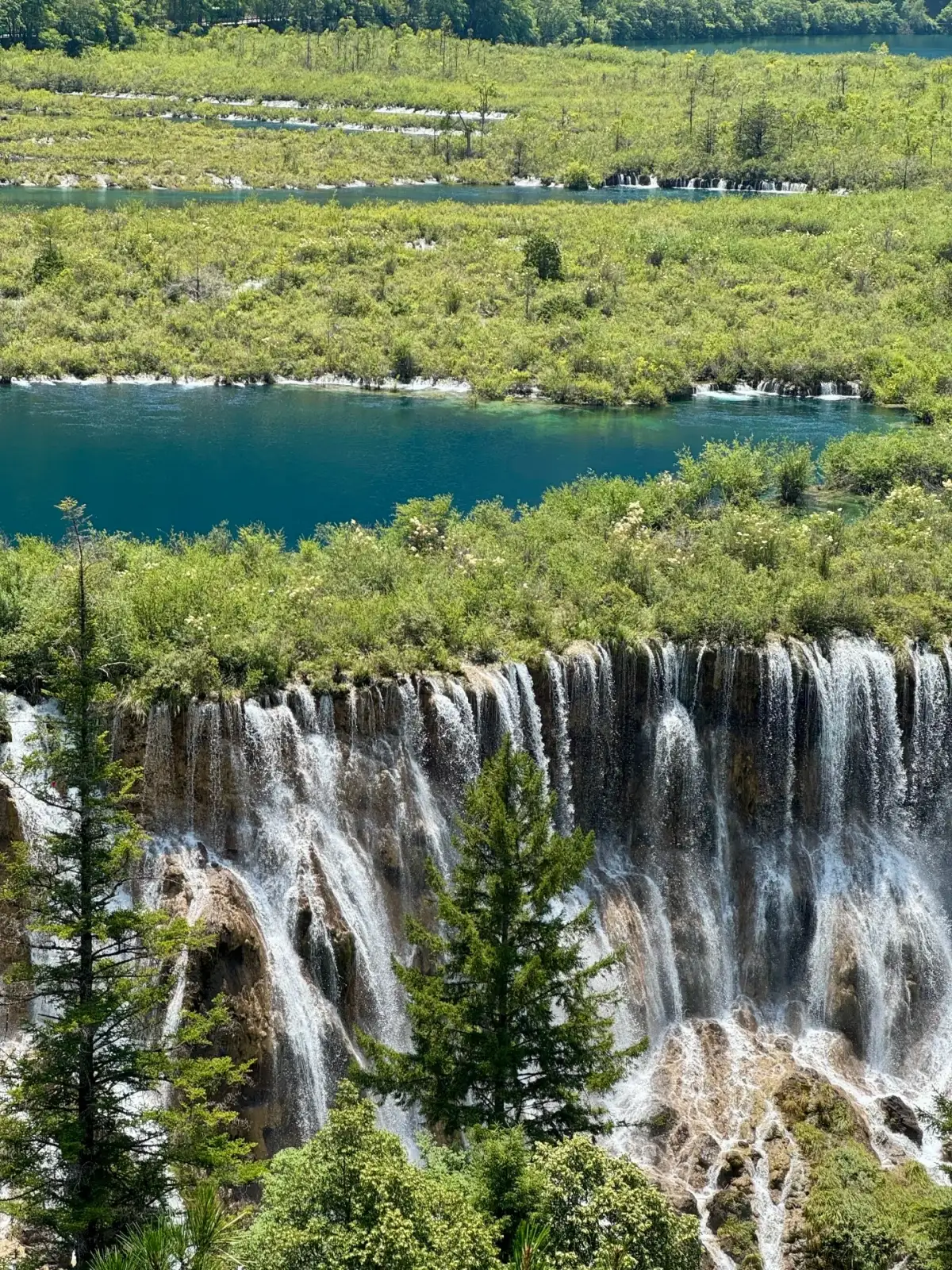 Water flows down the edges of elongated terraces, forming multiple waterfalls, with vegetation growing above.