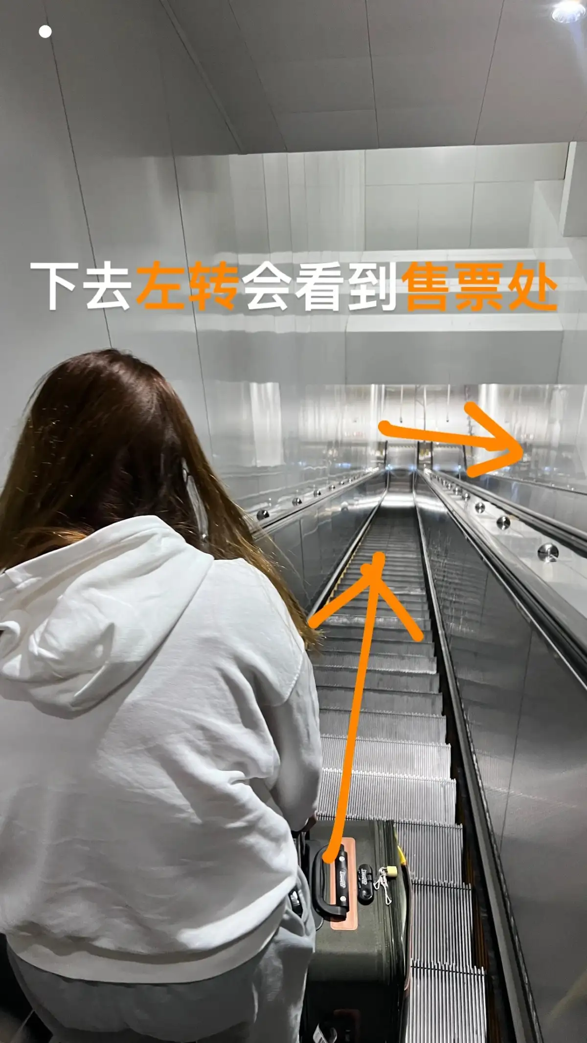 旅客背向镜头站在向下的自动扶梯上，画面带有路线箭头。