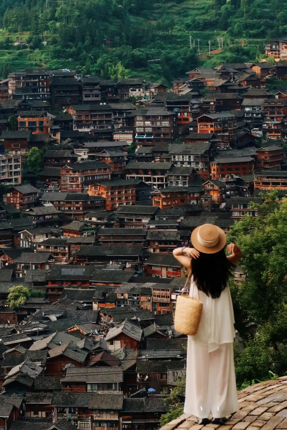A tourist’s silhouette in front of a wooden house at the Xijiang Thousand-Household Miao Village