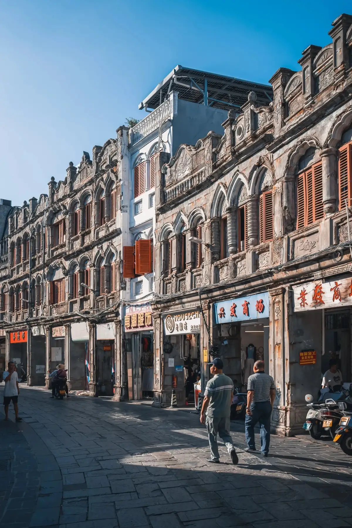 连续骑楼的拱廊、窗户与店铺招牌沿街排开,其中一段外墙呈浅蓝色。