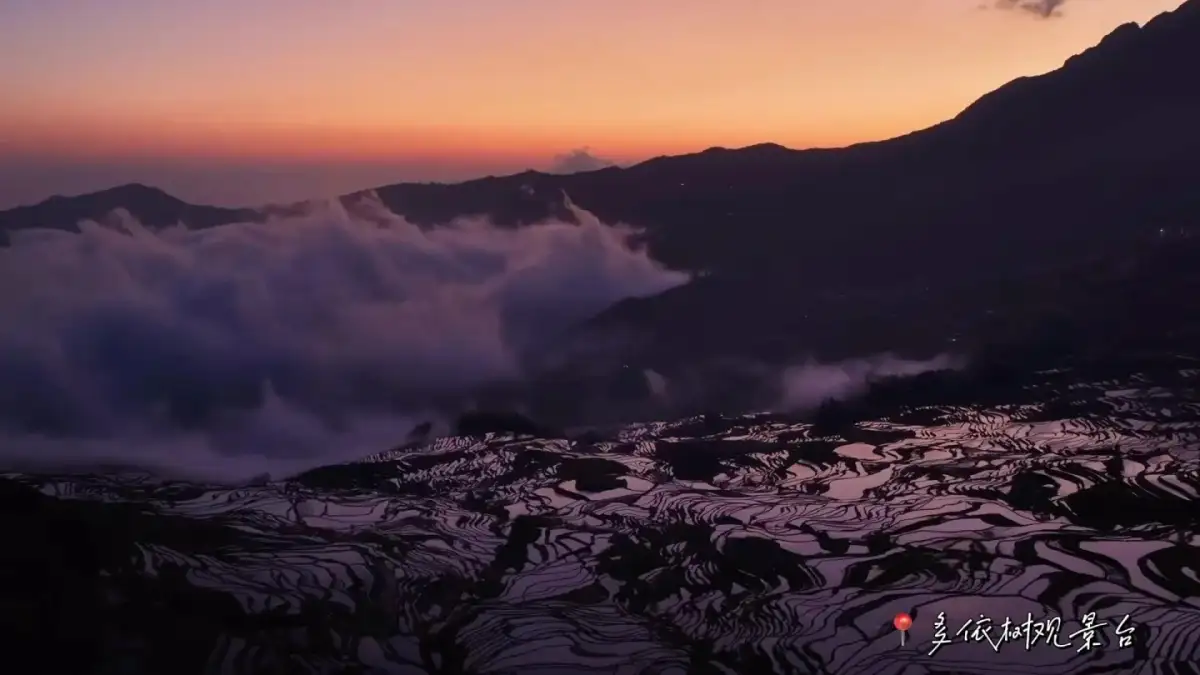 a sea of clouds, mountain silhouettes, and reflections on the terraced fields bathed in orange-red morning light