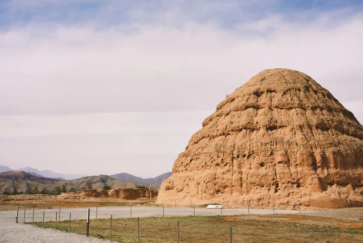 a towering earthen structure with layers of erosion patterns, surrounded by a low fence.