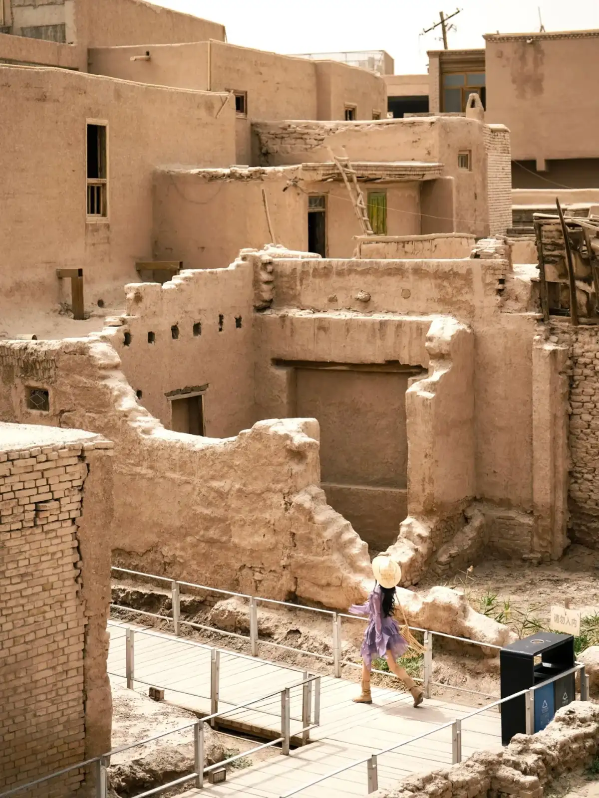 Earth-toned walls, doors, windows, and figures in the distance along the path within the fence