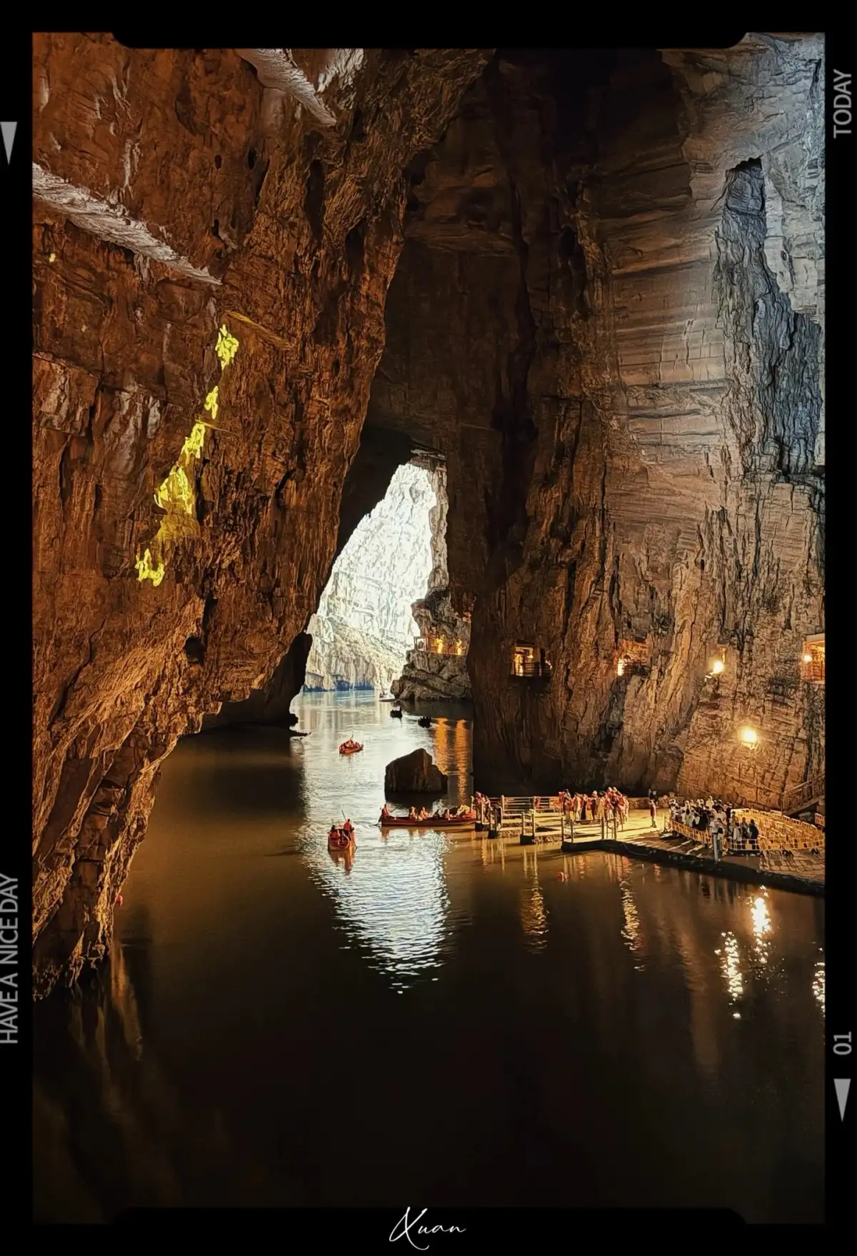 the water surfaces inside the cave reflect the towering rock walls and the bright cave openings in the distance