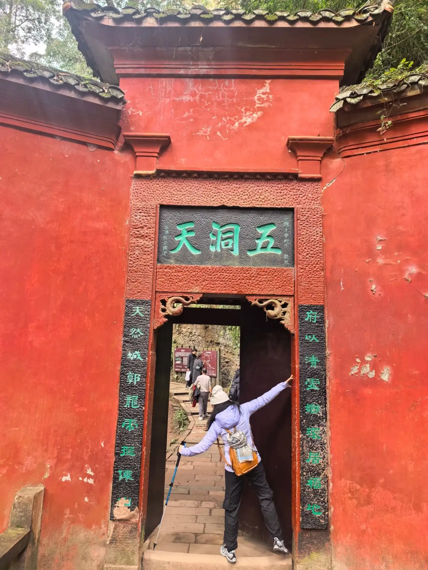 The red-walled gateways of the Five Caves of Mount Qingcheng and the silhouettes of tourists in the distance