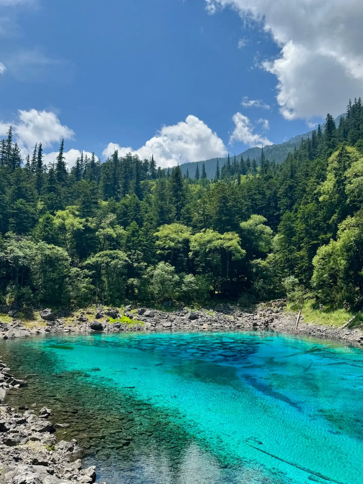 turquoise-blue lakes nestled against rocky shores, with forests, hillsides, and blue skies dotted with white clouds in the background.