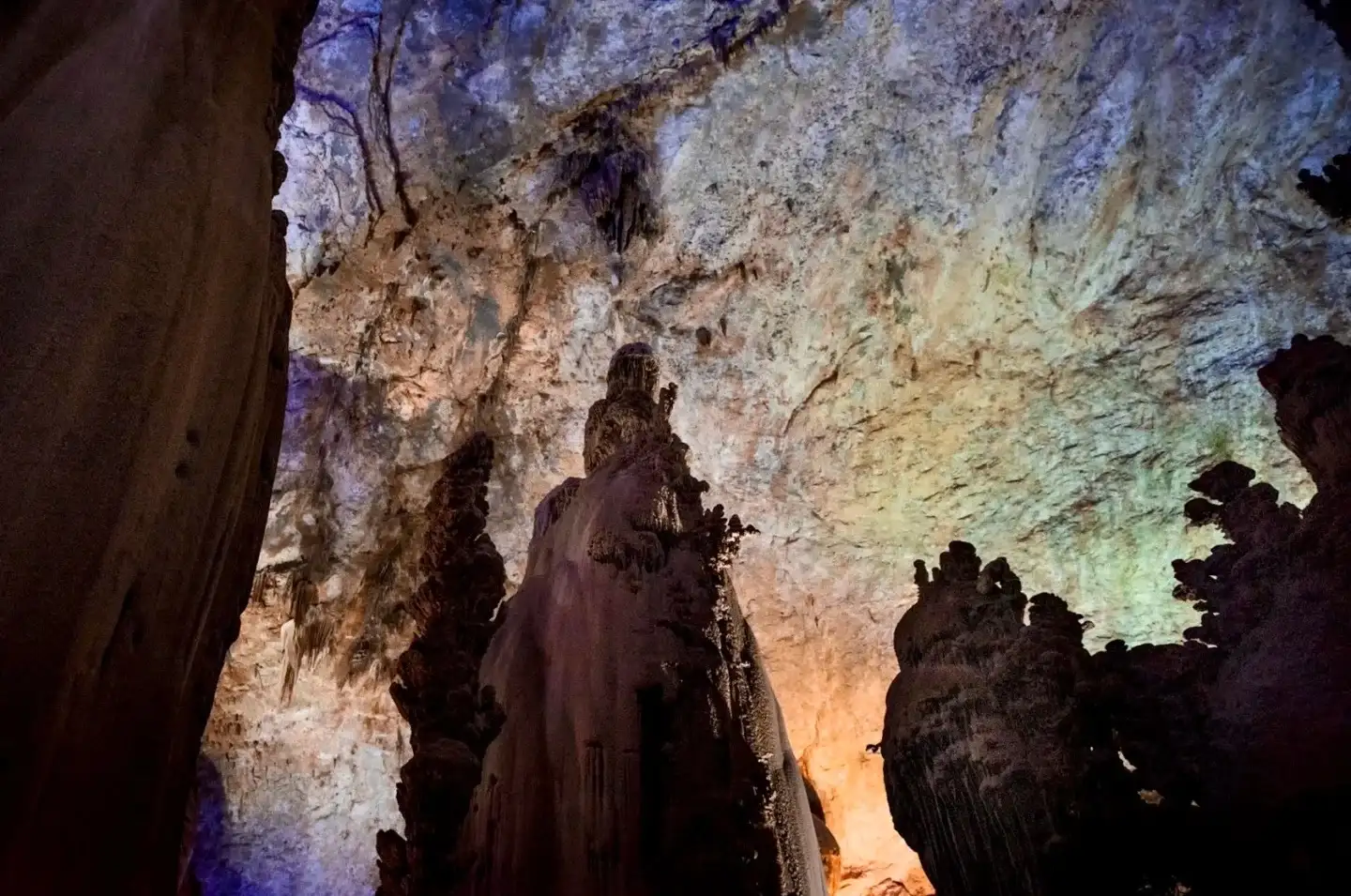 Looking up from below at the towering sedimentary formations and sunlit rock walls inside the cave
