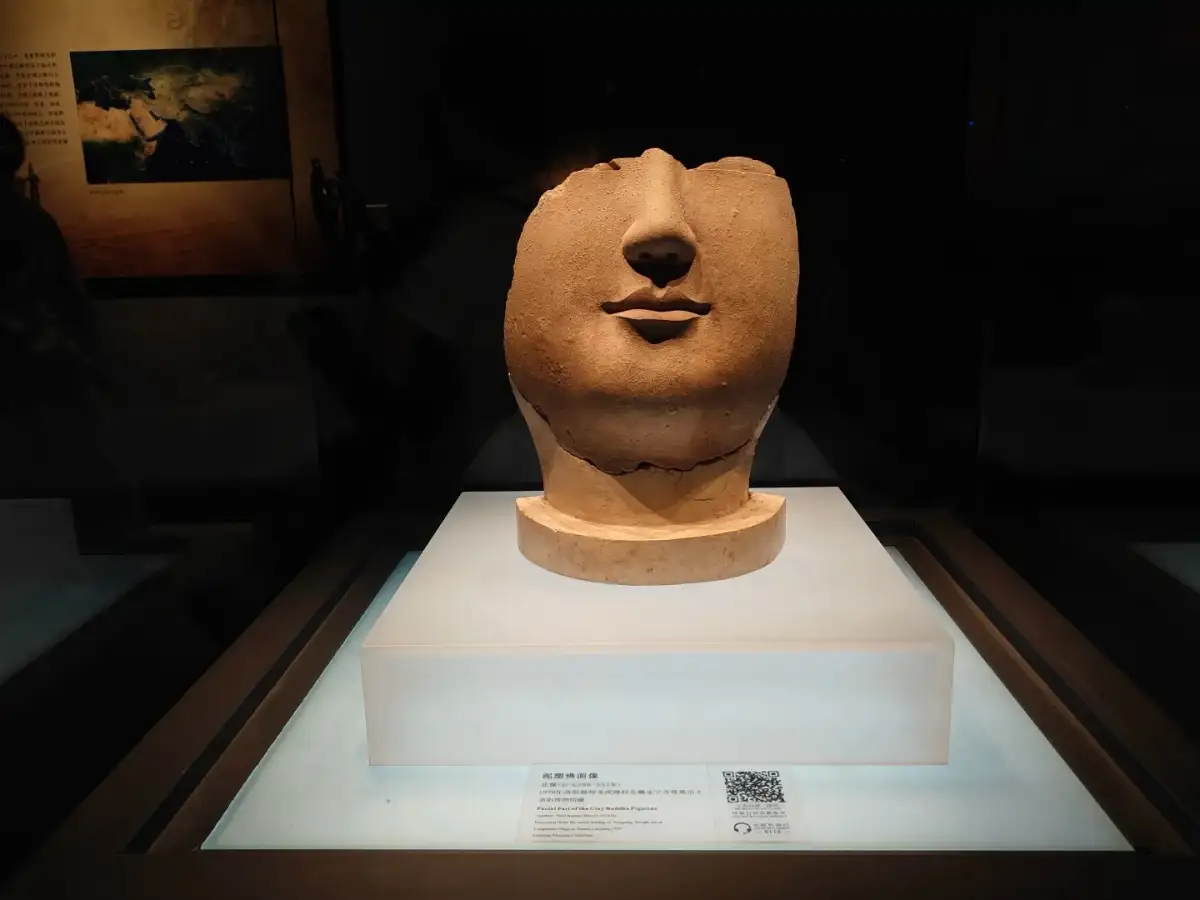 A fragmentary stone sculpture of a head is placed in the center of the display case, with an exhibit description attached below.