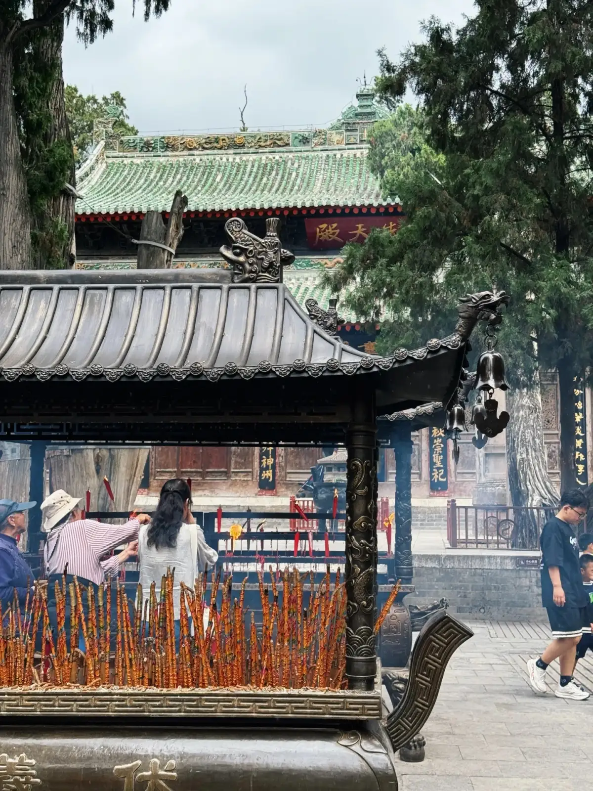 Incense burners filled with sticks of incense, gray-tiled eaves, and the green-tiled hall in the background