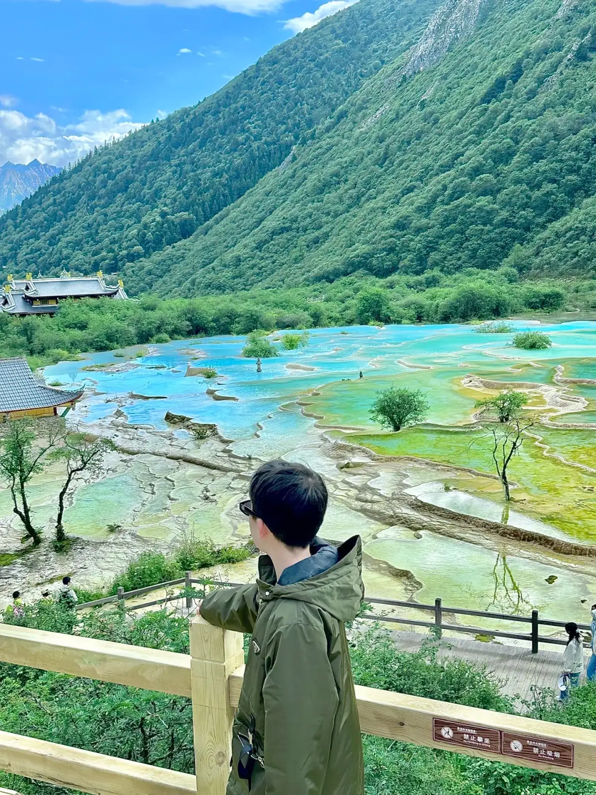 从木栏杆旁看黄龙彩池与山谷,前景是人物背影