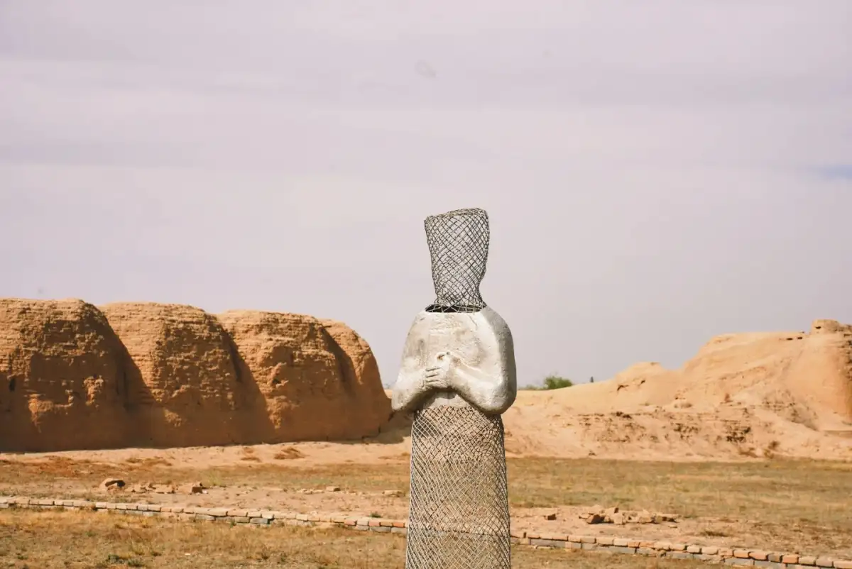 stone carvings of figures wearing tall hats and with hands crossed over their chests in the same frame as the earthen wall ruins.