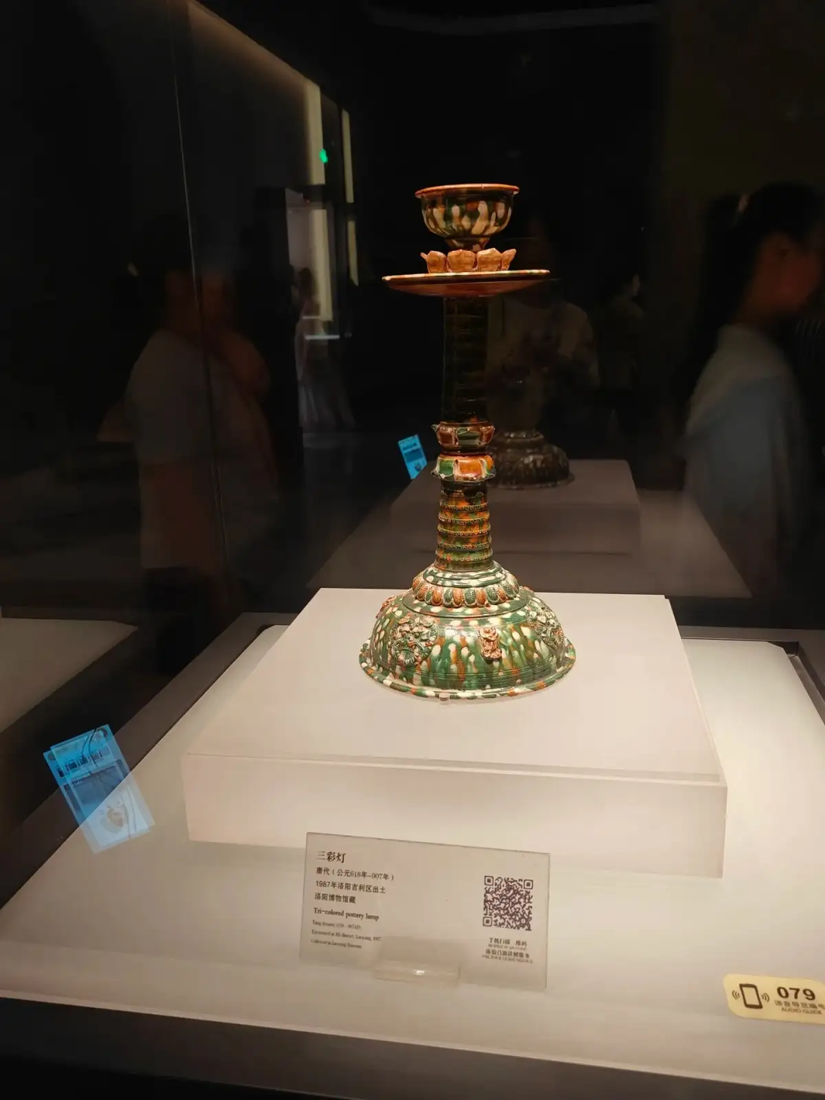 In a glass display case, a high-footed object with green decorations stands on a white display platform.
